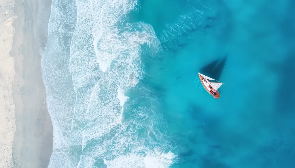 Barefoot Luxury Living Aerial view of sailing boat on turquoise waters reflecting the Naples waterfront lifestyle